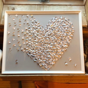 May include: A white frame with a gray background featuring a heart shape made of silver butterflies. The butterflies are arranged in a way that creates a 3D effect.