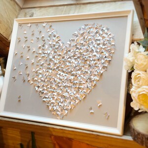 May include: A white frame with a gray background and a heart shape made of silver and white butterflies. The heart is centered in the frame.