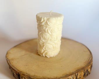 Può includere: Candela bianca a forma di pilastro con un motivo a rosa su una fetta di legno.