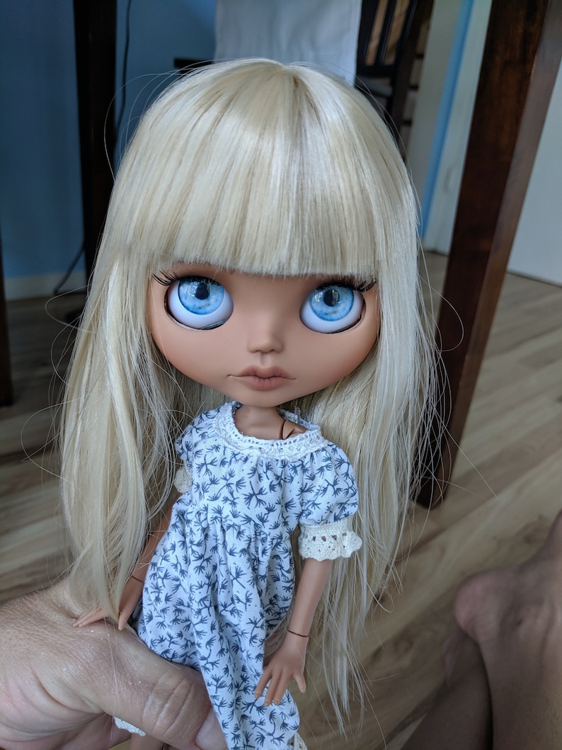 Puede incluir: Una mu&ntilde;eca con el pelo largo y rubio, ojos azules y un vestido blanco con estampado floral.