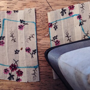 Puede incluir: Dos piezas de tela con un patr&oacute;n floral y una l&iacute;nea azul dibujada en ellas. Una plancha est&aacute; apoyada sobre una de las piezas de tela.