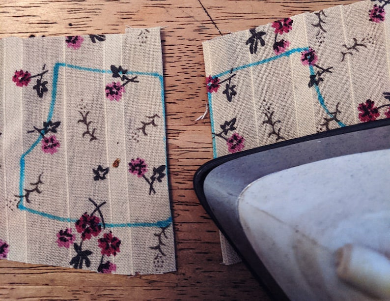 Puede incluir: Dos piezas de tela con un patr&oacute;n floral y una l&iacute;nea azul dibujada en ellas. Una plancha est&aacute; apoyada sobre una de las piezas de tela.