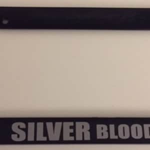Puede incluir: Marco de matrícula de plástico negro con el texto "SILVER BLOODED" en letras plateadas.