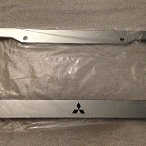 Pode incluir: Moldura de placa de licença prateada com um logotipo da Mitsubishi. A moldura é feita de metal e tem um acabamento liso.