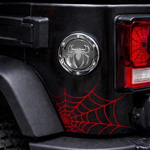Può includere: Veicolo nero con grafica a ragnatela rossa e un emblema di ragno cromato. Il fanale posteriore presenta un design a ragnatela rossa. La carrozzeria del veicolo ha una finitura opaca.