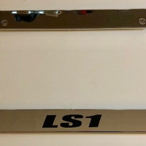 Puede incluir: Marco de matrícula cromado con letras negras que dicen "LS1".