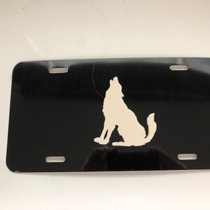 Puede incluir: Placa de matrícula de metal negro con una silueta blanca de un lobo aullando a la luna.