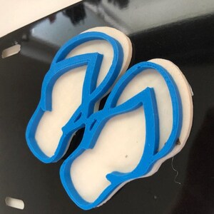 Könnte beinhalten: Zwei blaue Flip-Flop-Ausstecher auf einer schwarzen Oberfläche.