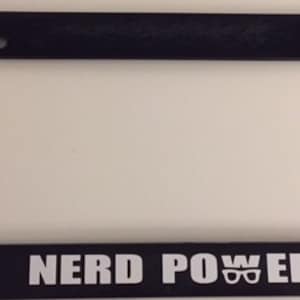 May include: Black plastic license plate frame with white text that reads "NERD POWER" and a pair of glasses icon.