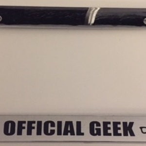 May include: A chrome license plate frame with the text "OFFICIAL GEEK" and a pair of glasses icon.