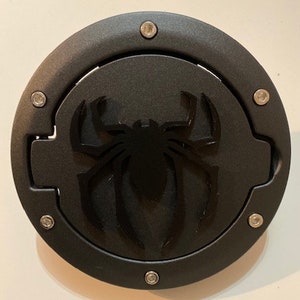 Può includere: Tappi per serbatoio di benzina nero con un design a silhouette di ragno. Il tappo è di forma circolare ed è realizzato in un materiale testurizzato. Ha un'apertura a cerniera ed è fissato con più viti.