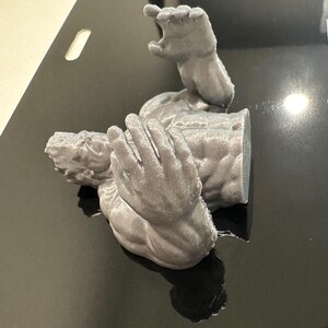 May include: A gray, 3D-printed sculpture of a torso with outstretched arms and hands. The sculpture has detailed musculature and is positioned as if reaching out. The object is made of a matte gray material.