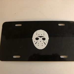 May include: Black license plate with a white silhouette of a hockey mask.