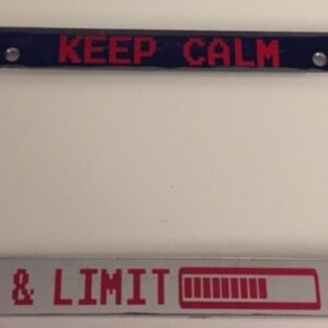 May include: Chrome license plate frame with a red and white graphic that says "KEEP CALM & LIMIT" with a red battery bar graphic.