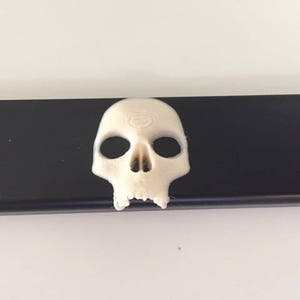 Puede incluir: Una escultura de calavera blanca sobre un fondo negro. La calavera tiene un diseño detallado y está hecha de un material liso.