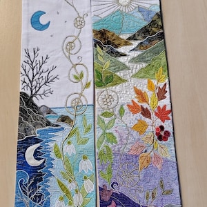May include: A white fabric stole featuring intricate embroidery. The left panel depicts a moonlit coastal scene with a bare tree and snowdrops. The right panel shows a sunlit mountain landscape with autumn leaves, flowers, and a thistle plant.