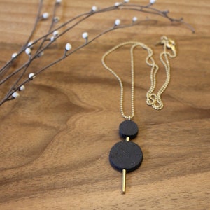 May include: A gold chain necklace with a black stone pendant. The pendant is made of two round black stones, one larger than the other, connected by a gold bar.