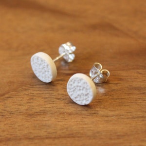 May include: A pair of white ceramic stud earrings with a textured surface. The earrings have silver posts and backs.
