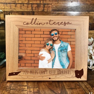 May include: A wooden photo frame with a personalized inscription "colin + teresa" and the text "727 miles can't keep us apart" with an outline of Tennessee and Ohio states. The frame features a photo of a couple smiling and wearing sunglasses.