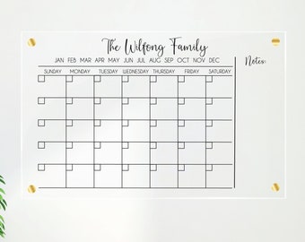 May include: A clear acrylic dry-erase calendar with gold push pins. The calendar is labeled "The Wilfong Family" and has spaces for each month of the year. It also has a section for notes.
