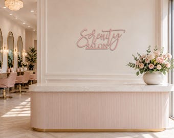 May include: A wall-mounted sign featuring the text Serenity Salon in a pink, cursive script font. The sign is displayed on a light-colored wall above a reception desk, positioned near a white vase filled with pink and white flowers.