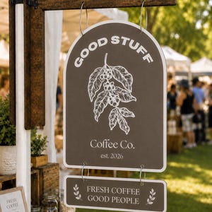 May include: A dark brown, arched hanging sign with white text reading GOOD STUFF, Coffee Co., est. 2026, and a white line drawing of a coffee branch. Below, a smaller rectangular sign reads FRESH COFFEE GOOD PEOPLE with leaf icons.