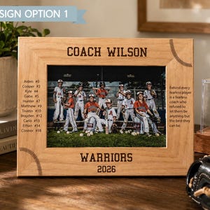 May include: A light-colored wooden picture frame featuring the engraved text COACH WILSON, WARRIORS, and 2026, with baseball stitching accents. The frame holds a photograph of a youth baseball team on a field, with a roster list and quote engraved.