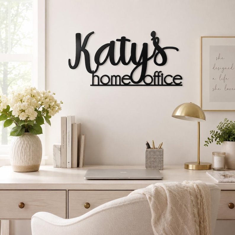 K&ouml;nnte beinhalten: Ein schwarzes Metall-Wandschild mit dem individuellen Schriftzug "Katy's home office" in einer Kombination aus Schreibschrift und serifenloser Typografie. Das Schild ist an einer Wand &uuml;ber einem Schreibtisch montiert und hat eine dunkle Oberfl&auml;che.