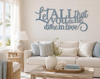 May include: A blue wall-mounted sign featuring the cursive and block letter text Let ALL that you do BE done in love. The sign is constructed from a flat material and is mounted on a white horizontal paneled wall above a sofa.