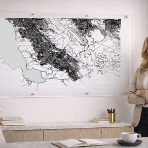 May include: A black and white map of a city, mounted on clear acrylic with gold-colored hardware. The map is detailed with roads and buildings. The map is displayed in a well-lit room.