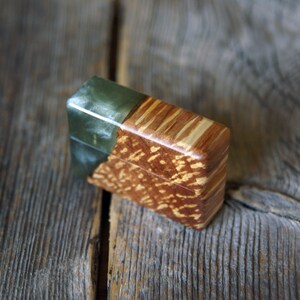 May include: A rectangular wooden box with a green, translucent top. The box's body is a warm brown with a speckled pattern. The wood grain is visible, adding texture. The box is set against a rustic wooden surface.