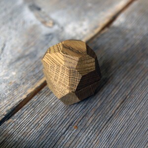 May include: A wooden ring box with a geometric design. The box is made of light brown wood and has a natural finish.