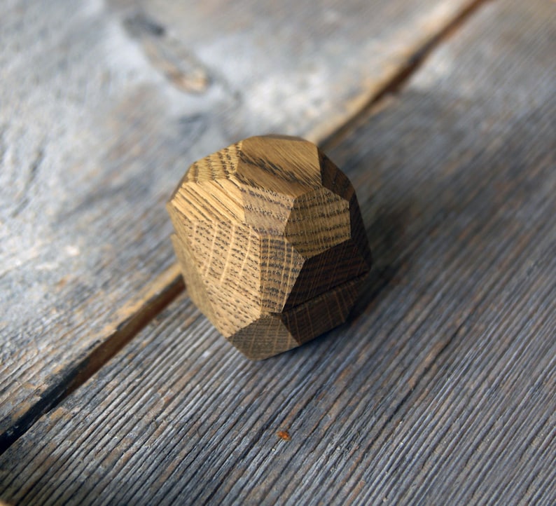 May include: A wooden ring box with a geometric design. The box is made of light brown wood and has a natural finish.