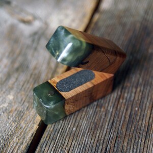 Peut inclure: Une boîte en bois avec un couvercle à charnière, combinant du bois clair et des accents de pierre vert foncé. La boîte est ouverte, révélant un intérieur gris foncé. La boîte repose sur une surface en bois vieilli.