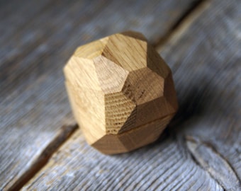 May include: A wooden ring box shaped like a geometric diamond. The box is made of light brown wood and has a smooth, polished finish.