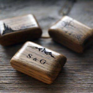 Könnte beinhalten: Drei Holzkästchen für Ringe mit gravierten Designs. Die erste Box hat ein Bergpanorama-Design und die Initialen "S & G". Die zweite Box hat ein Kompass-Design und das Wort "Immer". Die dritte Box hat ein Schloss-Design.