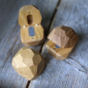 May include: Three wooden ring boxes in the shape of a diamond. The boxes are made of light brown wood and have a hinged lid. The boxes are open and show the interior of the boxes, which are lined with a dark gray material.