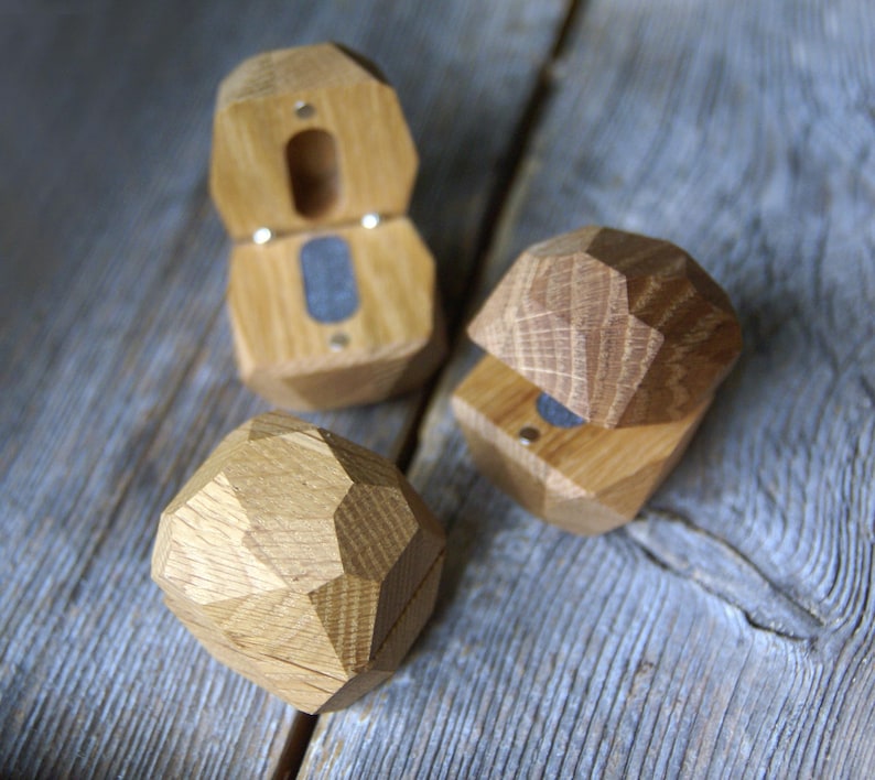 May include: Three wooden ring boxes in the shape of a diamond. The boxes are made of light brown wood and have a hinged lid. The boxes are open and show the interior of the boxes, which are lined with a dark gray material.
