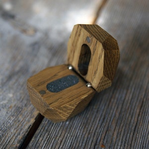 May include: A wooden ring box with a hinged lid, made of light brown oak wood. The box is open, revealing a gray felt lining inside.