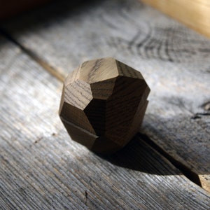 May include: A wooden geometric shape with a rough, textured surface. The shape is a dark brown color and has multiple facets.