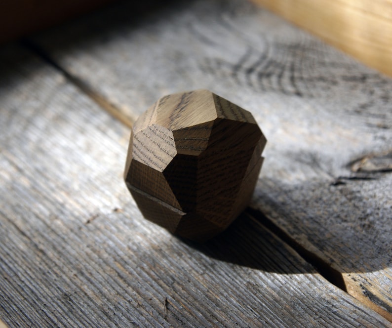 May include: A wooden geometric shape with a rough, textured surface. The shape is a dark brown color and has multiple facets.