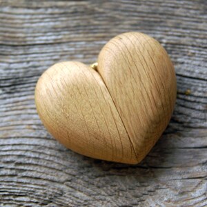 May include: A wooden heart-shaped box with a natural wood grain finish. The box is open and appears to be made of two halves.