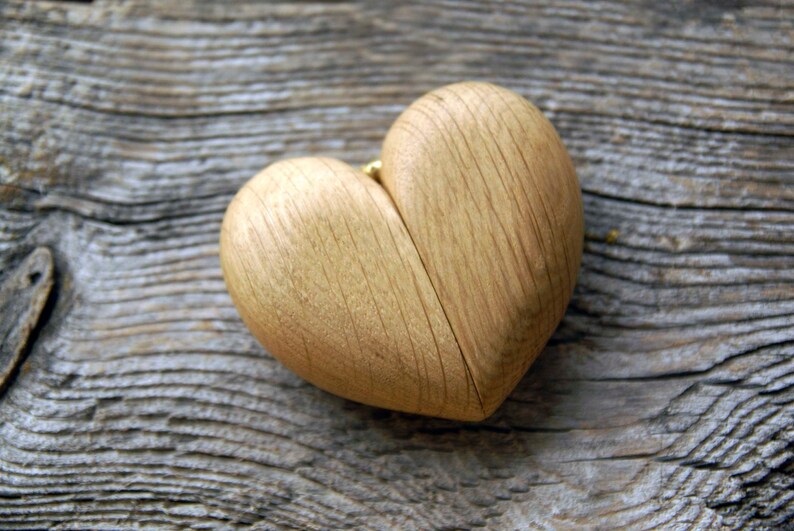 May include: A wooden heart-shaped box with a natural wood grain finish. The box is open and appears to be made of two halves.