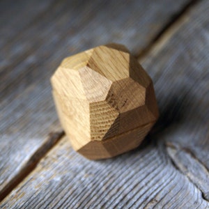 May include: A wooden ring box shaped like a geometric diamond. The box is made of light brown wood and has a smooth, polished finish.