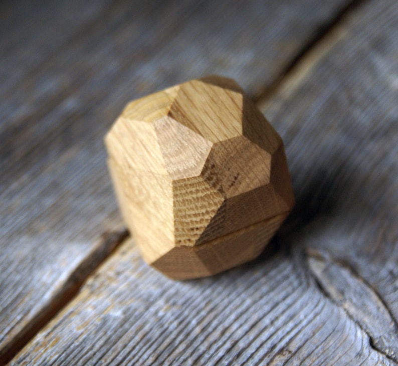 May include: A wooden ring box shaped like a geometric diamond. The box is made of light brown wood and has a smooth, polished finish.