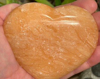 May include: A heart-shaped orange carnelian crystal with a smooth, polished surface. The crystal has a swirling pattern of light and dark orange hues.