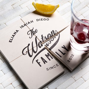 Puede incluir: Cuatro posavasos cuadrados blancos con texto negro. Los posavasos están dispuestos en forma de cuadrado. El texto en los posavasos dice "The Watson Family Since 2012" e incluye los nombres "Eliana", "Isaiah" y "Diego".