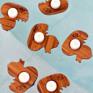 Op de afbeelding: Vijf houten kaarshouders in de vorm van eenden met de initialen "CBB" gegraveerd op elk. Elke houder heeft een kleine witte theelichtkaars.