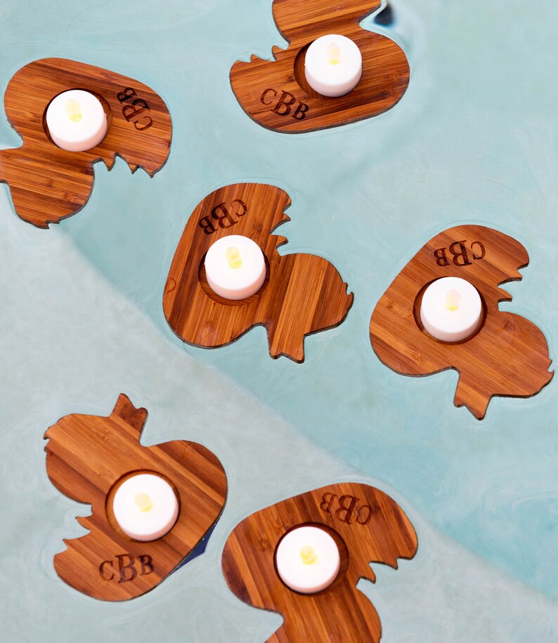 Op de afbeelding: Vijf houten kaarshouders in de vorm van eenden met de initialen "CBB" gegraveerd op elk. Elke houder heeft een kleine witte theelichtkaars.
