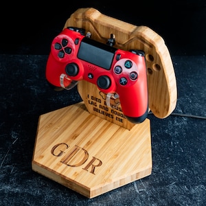 May include: A red video game controller sits on a wooden stand with the initials "GDR" engraved on the front. The stand is shaped like a video game controller and has the text "I died because of lag and nobody believes me" engraved on the back.